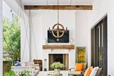 a lovely modern farmhouse terrace with a fireplace, a suspended daybed, modern chairs, potted plants and blooms and a wooden chandelier