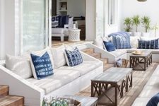 a lovely seaside terrace with built-in white sofas, blue pillows, coffee tables and woven pendant lamps is a great psace to relax in