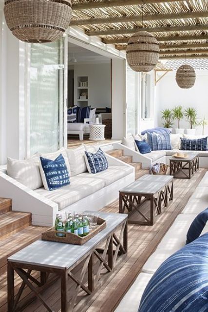a lovely seaside terrace with built in white sofas, blue pillows, coffee tables and woven pendant lamps is a great psace to relax in
