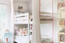 a lovely shared girls’ bedroom with a built-in bookcase and a bunk bed, pastel and white bedding, a coral rug and a blue nightstand