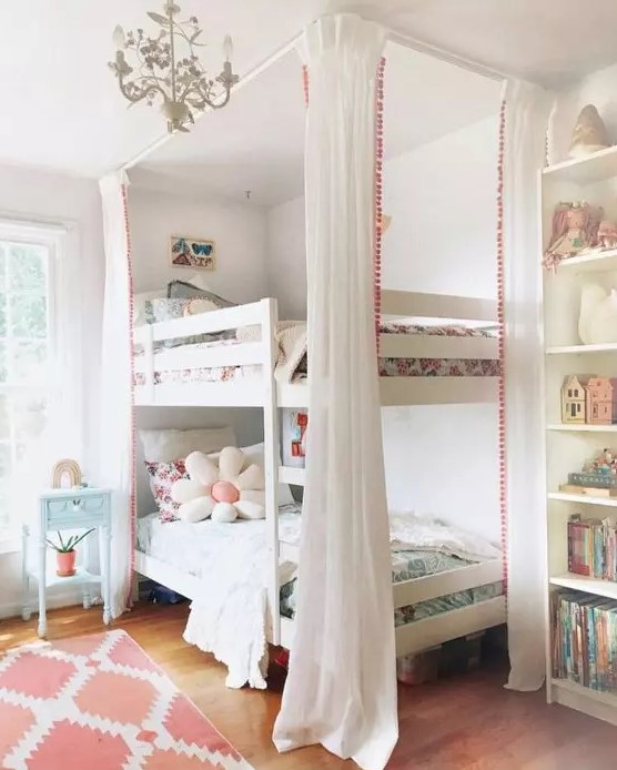 a lovely shared girls' bedroom with a built-in bookcase and a bunk bed, pastel and white bedding, a coral rug and a blue nightstand