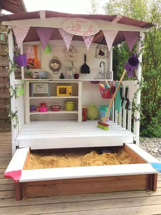 a lovely shed with toy tableware and other stuff, with buntings and greenery plus a sand box is a geat idea
