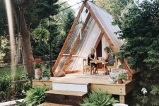 a lovely teepee-style playhouse with glass panels, a porch with potted blooms is a cool solution for a boho or modern backyard