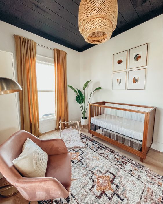 a mid-century modern nursery with a black ceiling, a printed rug, a pink chair, a wood and acryl crib and mustard curtains