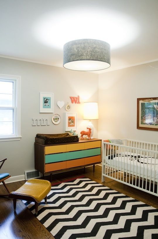 a mid-century modern nursery with a colorful dresser, a white crib with neutral bedding, a black and white printed rug and a gallery wall
