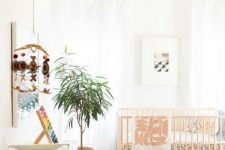 a mid-century modern nursery with neutral walls, a bold printed rug and bedding, a wooden pendant lamp and a pouf and a white dresser