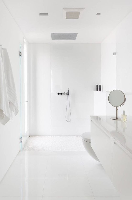 a minimal white bathroom clad with large scale tiles, a floating vanity, a frosted glass window, some mirrors
