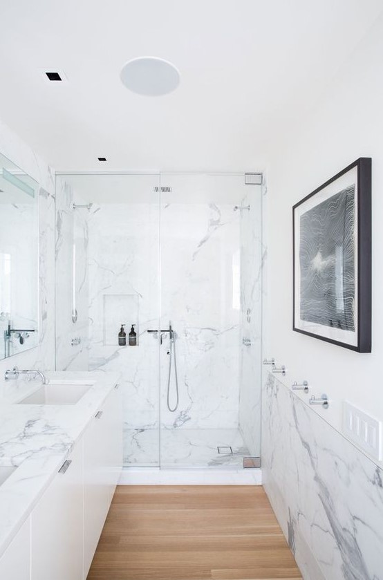 a minimalist bathroom clad with white marble, with a large floating vanity, a statement artwork