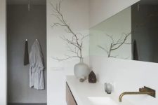 a minimalist bathroom done with white concrete, with a grey concrete floor, a long wooden vanity and a long and narrow mirror plus lights over it