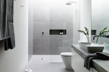 a minimalist grey and white bathroom with large scale tiles, a long vanity with a concrete countertop and a skylight over the shower