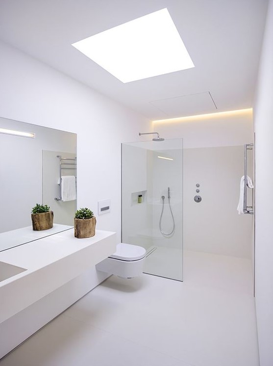 a minimalist white bathroom with a skylight, a floating vanity, a seamless glass shower space and built in lights