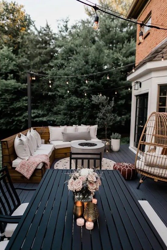 a modern and bold farmhouse terrace with a black deck, a built in bench with upholstery, a rattan egg chair, a black planked dining set