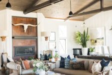 a modern barn living room with a built-in fireplace, grey and creamy sofas, a stained coffee table and dark-stained wooden beams