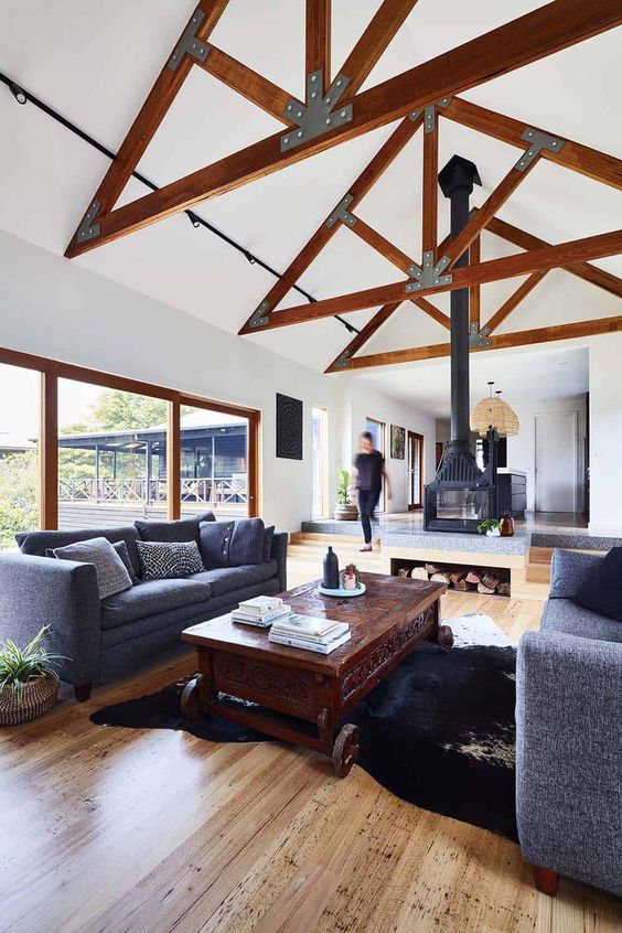 a modern barn living room with stained beams, graphite grey sofas, a dark-stained coffee table and a double-sided hearth