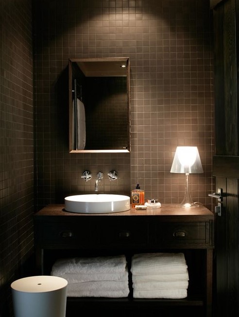 a modern chocolate powder room with tiles all over, a wooden vanity and touches of white, appliances and towels