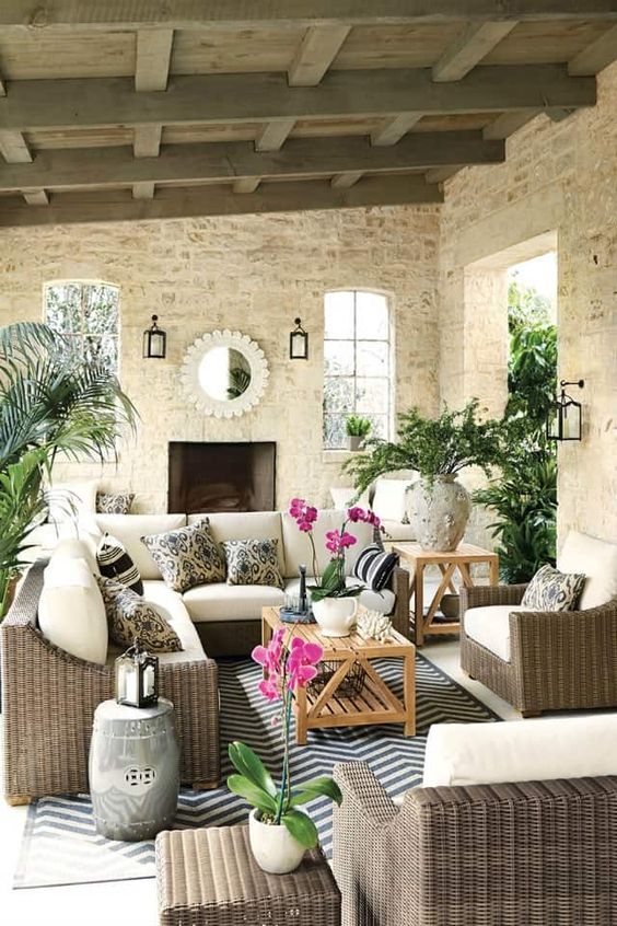 a modern farmhouse outdoor living room with taupe wicker furniture, stained tables, printed pillows, potted plants and a fireplace
