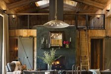 a moody barn living room with wooden walls and a ceiling, grey seating furniture, neutral textiles, pendant lamps, a built-in fireplace