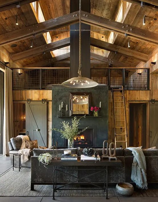 a moody barn living room with wooden walls and a ceiling, grey seating furniture, neutral textiles, pendant lamps, a built-in fireplace