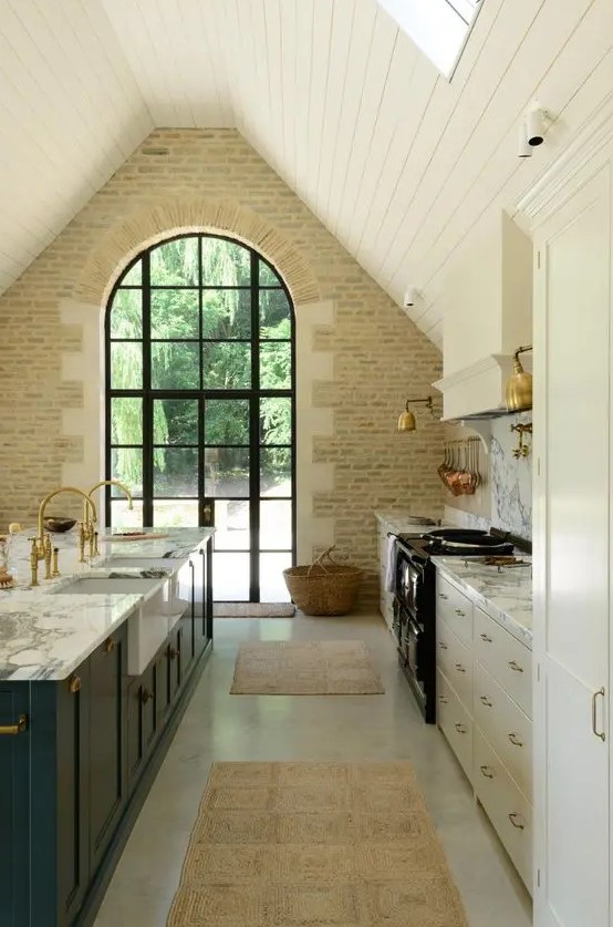 a neutral barn kitchen with white cabinets, a teal kitchen island, white marble countertops and a white stone wall