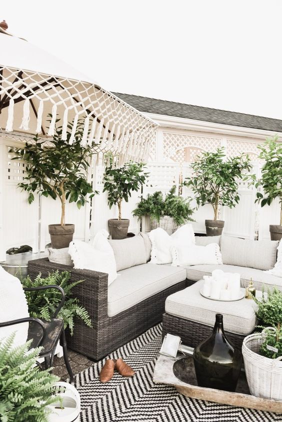 a neutral modern farmhouse meets boho terrace wiht dark wicker furniture, potted plants, neutral upholstery and tassels