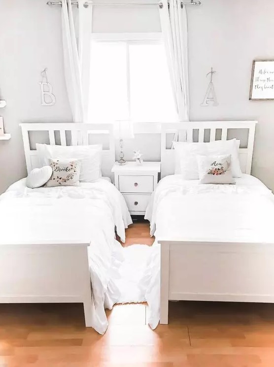 a neutral shared girls' bedroom with white beds and a nightstand, white curtains and bedding is a very airy and dreamy idea