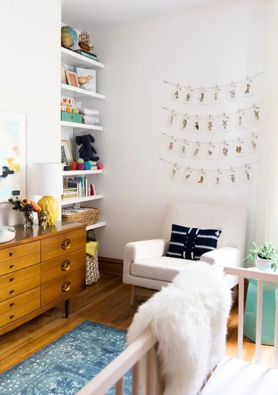 a pretty and cozy neutral nursery with open built in shelves, a stained credenza for storage, a creamy chair, a white crib and printed textiles