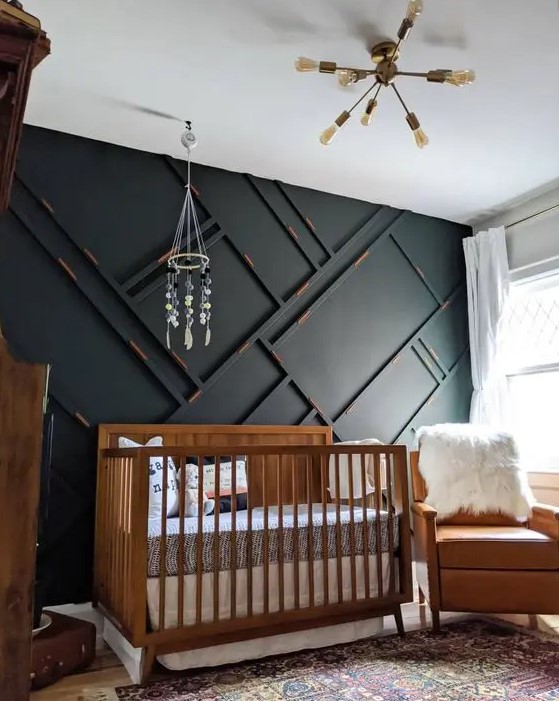 a pretty and small mid century modern nursery with a black paneled wall, a stained crib, an amber leather chair, neutral textiles, a chandelier and a mobile