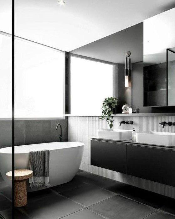 a refined Scandinavian bathroom with skinny white and large scale black tiles, a black double vanity, an oversized mirror and a cork stool by the tub