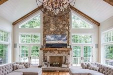a refined barn living room with a fireplace clad with stone, grey vintage sectionals, leather chairs, a sphere crystal chandelier
