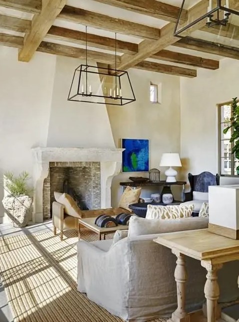 a refined barn living room with wooden beams, a fireplace clad with brick, neutral seating furniture, metal chandeliers and blue touches
