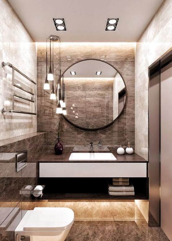 a refined brown bathroom with tiles, built in lights, pendant lamps and a round mirror