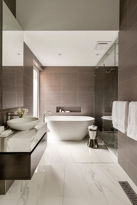 a refined contemporary bathroom clad with brown tiles and white marble tiles on the floor, an oval tub, a floating vanity with a bowl sink