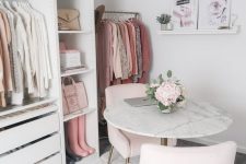 a romantic cloffice with a white makeshift closet, a crystal chandelier, some artworks, blush chairs and a marble table
