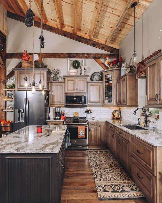 a rustic barn kitchen with wooden beams, stained cabinetry, a dark-stained kitchen island, stone countertops, pendant lamps