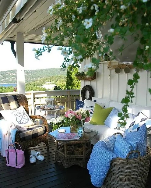 a rustic sea porch with wicker furniture, a bench with white upholstery, bright textiles and potted plants and blooms