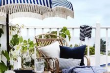 a seaside terrace with a wooden deck, rattan and wooden furniture, bright blue textiles, rope and some greenery