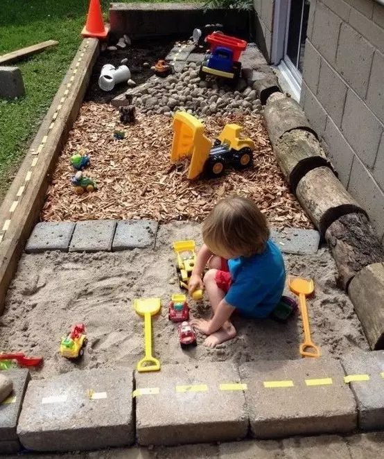 a simple outdoor oasis with a sand box, pebbles and a toy space is built of usual materials that most of have at hand