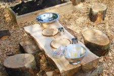 a simple rustic place space with a sand box, a wooden table and tree stump stools plus some metal tableware to play with