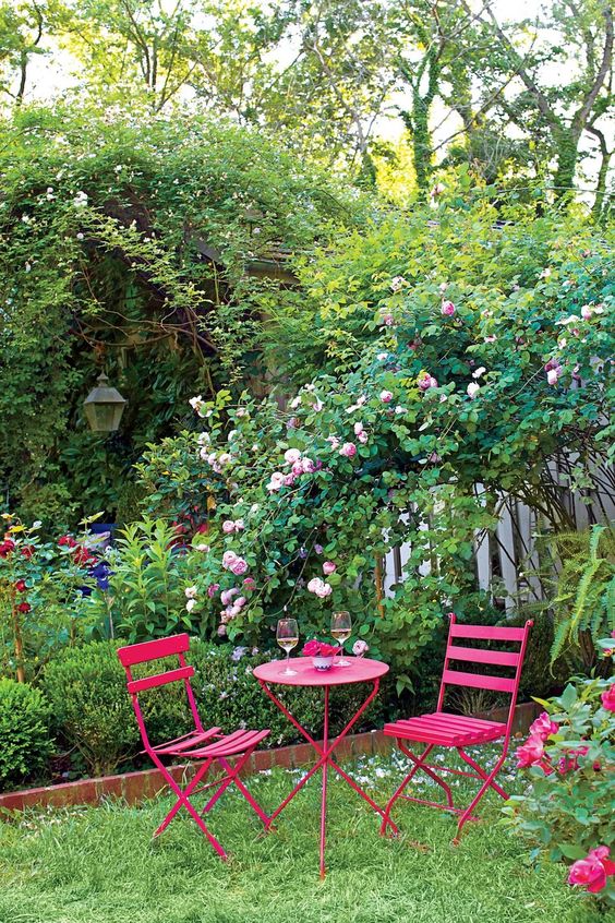 a small and bright garden dining space with hot pink furniture, a lawn and some blooming branches over this space is wow