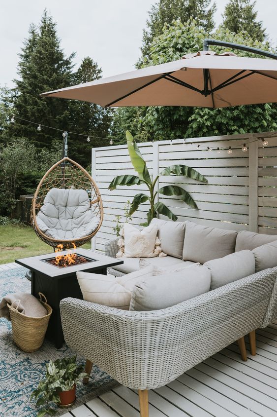 a small and cool farmhouse patio with a neutral wicker corner sofa, a fire pit, a pendant egg chair and a potted plant