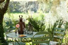 a small and cozy garden dining area wiht simple green metal furniture is located under the tree and is very inviting