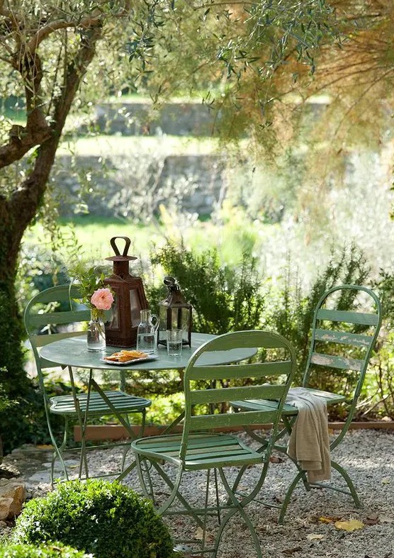 a small and cozy garden dining area wiht simple green metal furniture is located under the tree and is very inviting