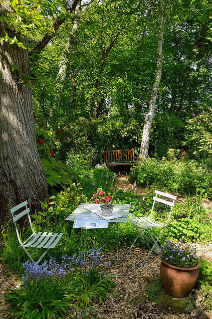 a small and cute garden dining nook in the greens, with simple folding furniture, a tree and blooms around invites you in