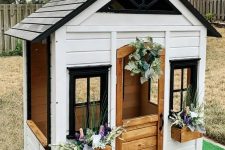 a small black and white farmhouse style playhouse with a stained half door and potted plants will be a nice idea for kids