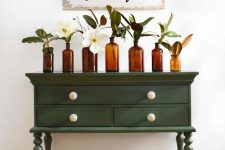 a small green vintage dresser with an arrangement of apothecary bottles with neutral blooms and a sign over it for styling a rustic space