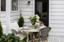 a small modern farmhouse terrace with mosaic tiles, vintage and modern wooden and rattan furniture, potted plants and blooms and lights over the space