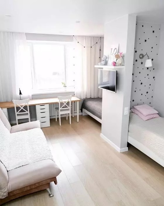 a small shared kids' bedroom with beds by the walls and a space divider, a double desk with chairs and a sofa plus a TV