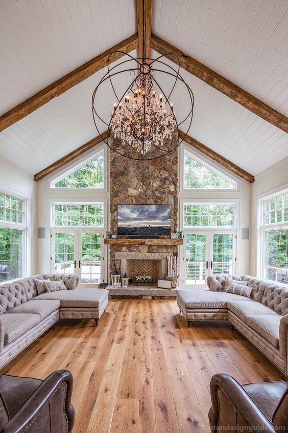 a sophisticated barn living room with a stone and brick fireplace, a crystal sphere chandelier, grey sectionals and leather chairs