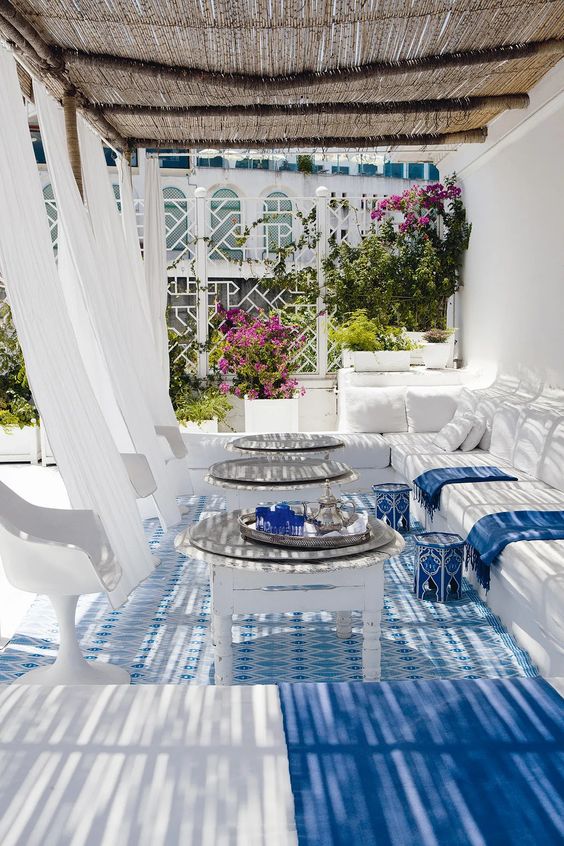 a sophisticated blue and white beach terrace with curtains, modern furniture, low coffee tables and blue painted stools, a printed rug