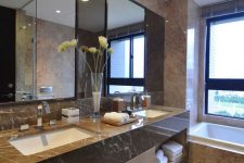 a sophisticated minimalist bathroom clad with brown marble tiles and a large shared vanity, a large mirror